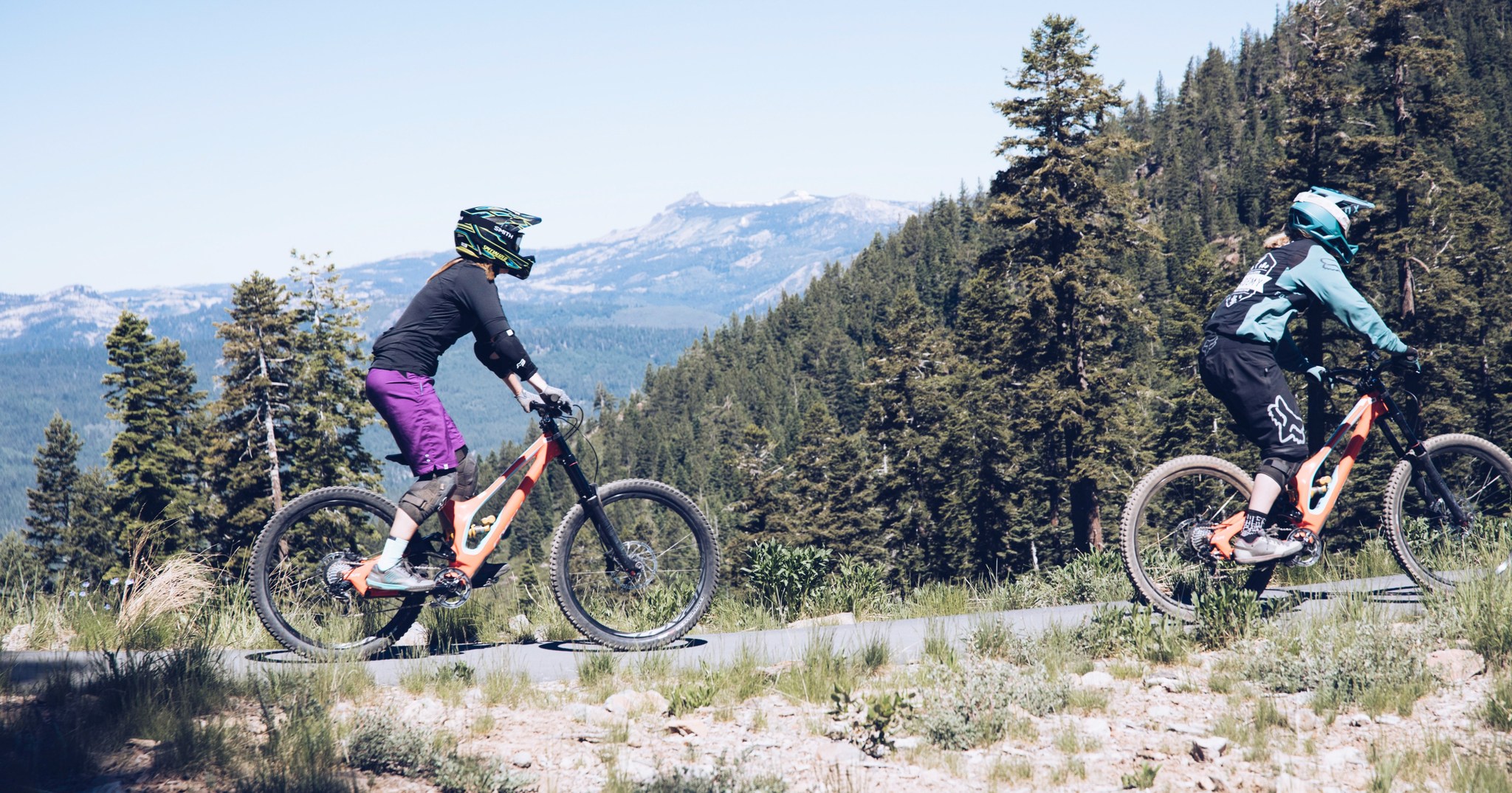 two people riding mountain bikes with a mountain and trees